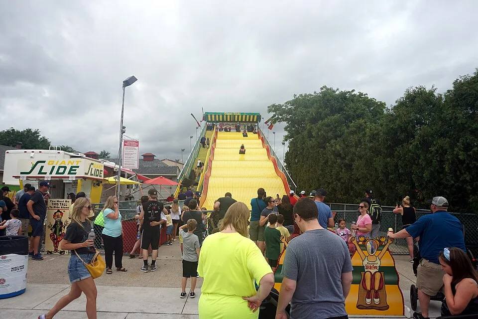 Tall yellow Super Slide carnival attraction with riders — giant slide rental for school carnivals Los Angeles